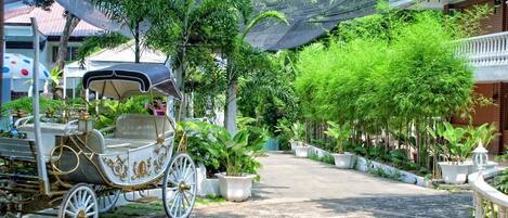 A carriage parked on a paved path surrounded by lush greenery and potted plants.