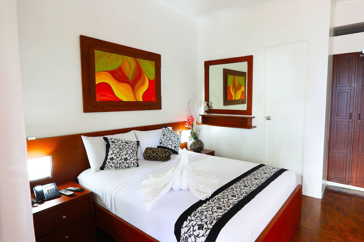 A hotel room with a neatly made bed, a bedside telephone, a vase with flowers, and artwork on the walls.