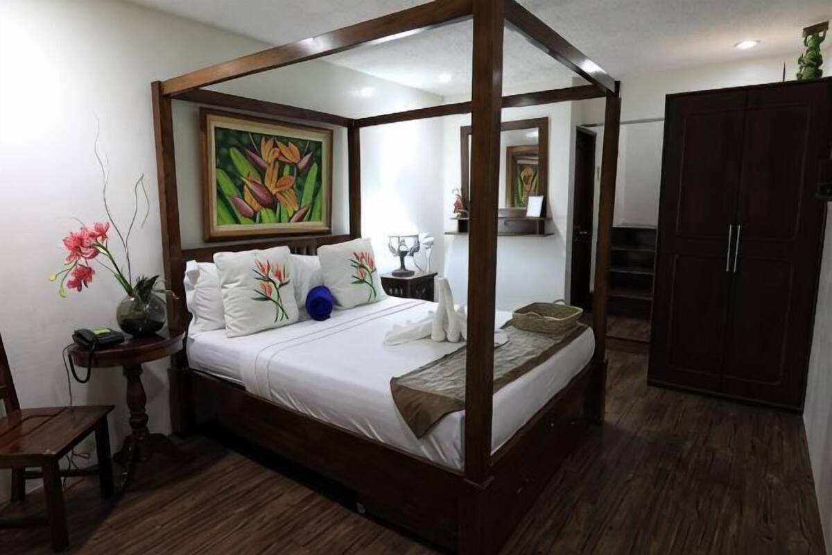 A four-poster bed with a nightstand, a mirror, a wardrobe, and a painting on the wall.