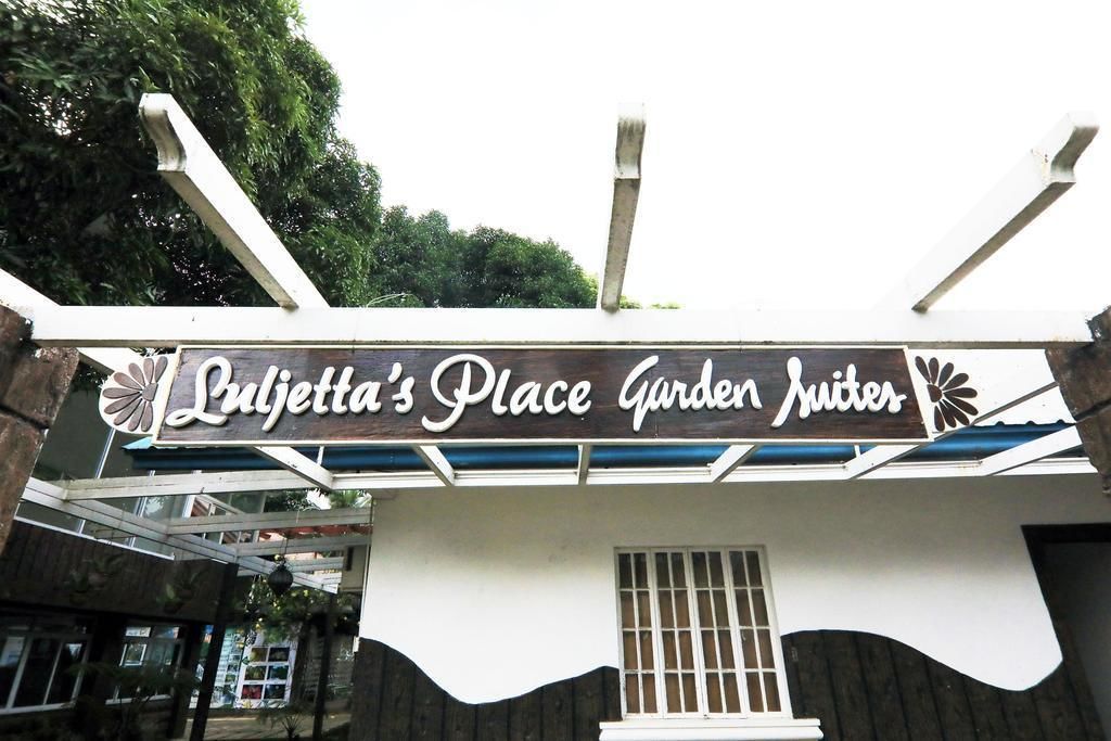 A sign for 'Lujetta's Place Garden Suites' with a modern design and a view of the surrounding area.