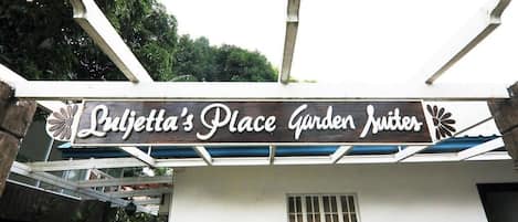 A sign for 'Lujetta's Place Garden Suites' with a modern design and a view of the surrounding area.