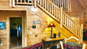 A wooden cabin interior with a staircase, a sofa, a lamp, and a sign indicating it's a cabin rental.