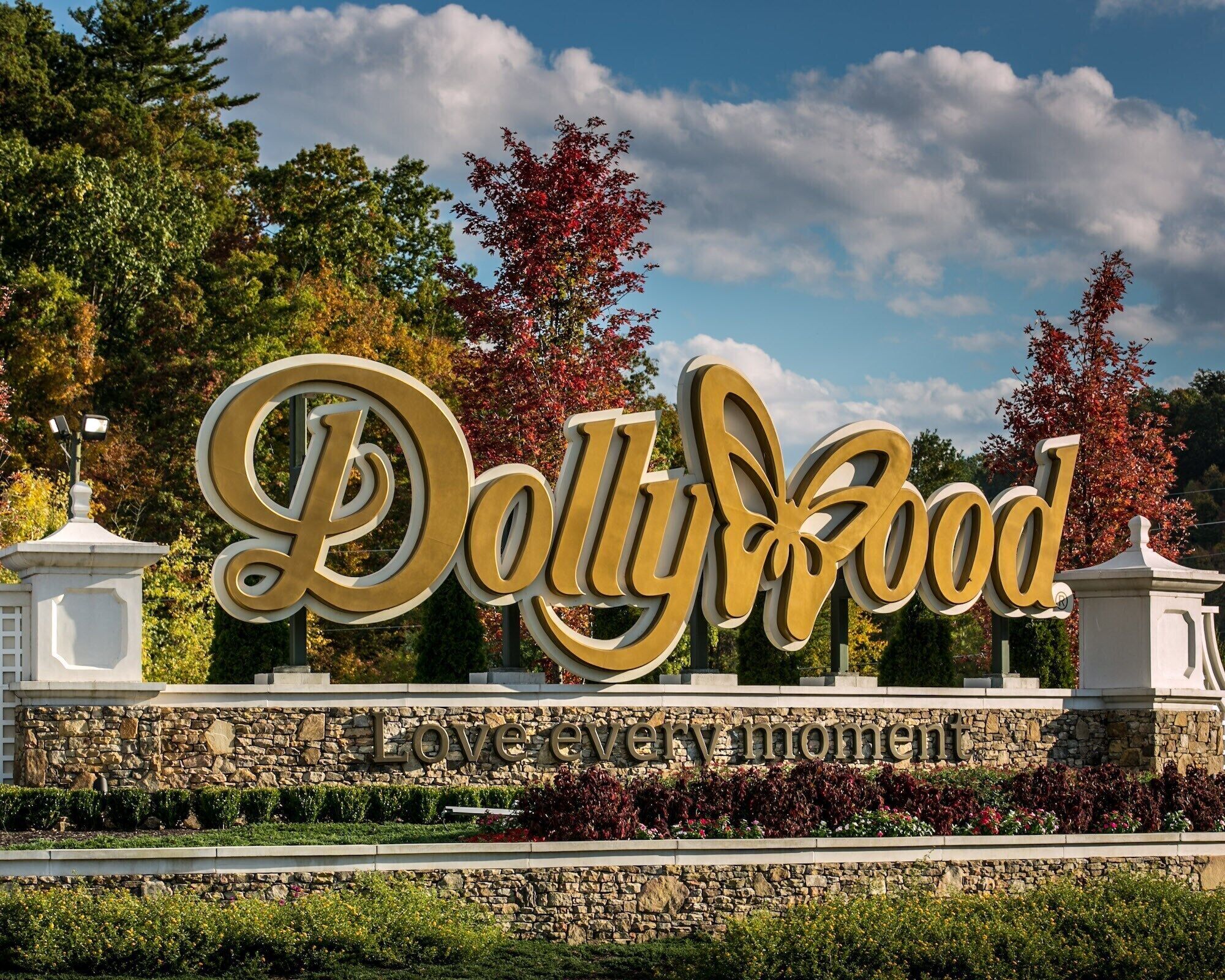 A sign for 'Polly Wood' with a stone wall and flower beds in front.