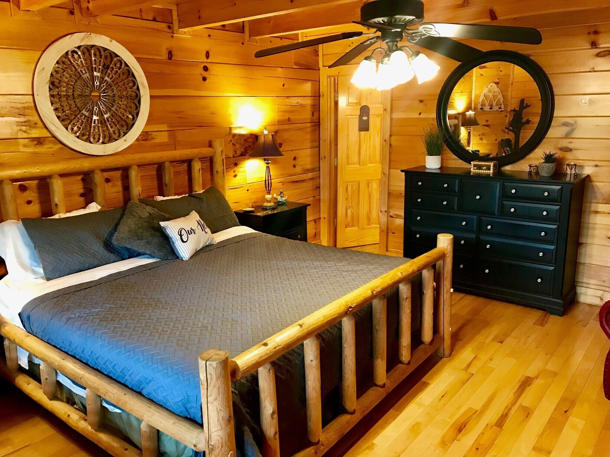 Een slaapkamer in een houten chalet, met een bed, een dressoir, een spiegel, een plafondventilator en een dartbord.