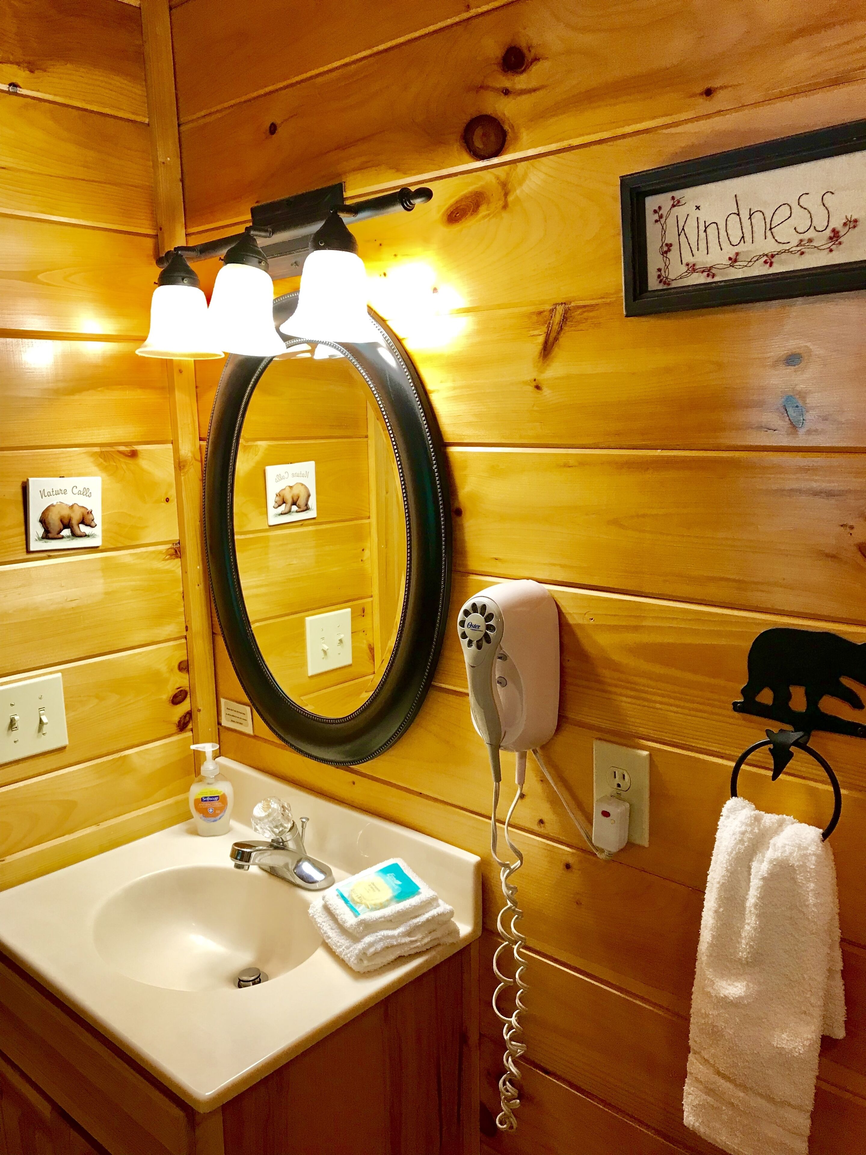 A wooden cabin bathroom with a sink, mirror, hairdryer, and a towel rack.
