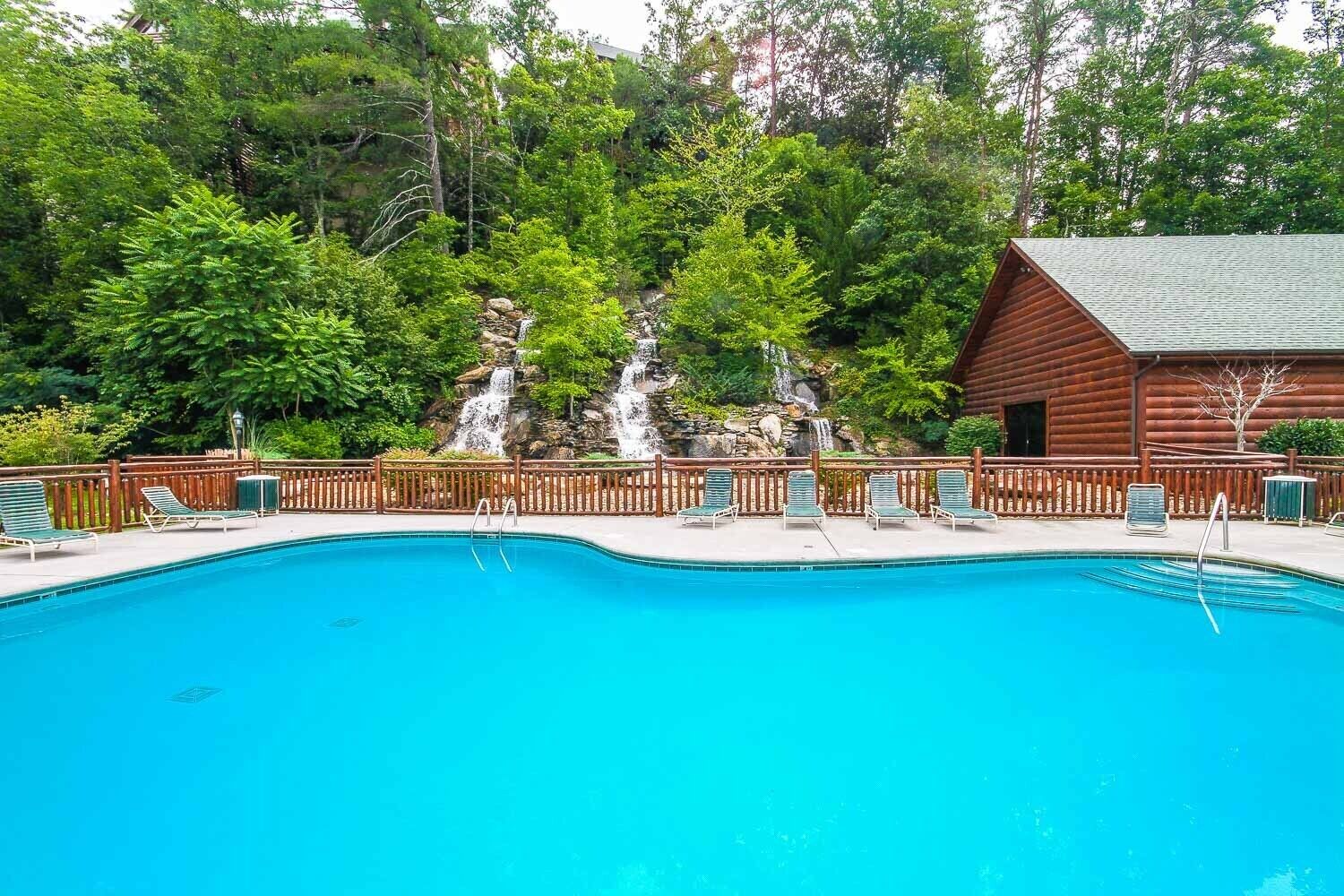 Une piscine d’un bleu éclatant, avec des chaises longues et un chalet en bois en arrière-plan.