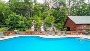 A clear blue pool with lounge chairs and a wooden cabin in the background.
