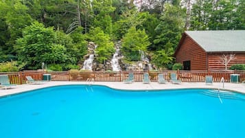 Une piscine d’un bleu éclatant, avec des chaises longues et un chalet en bois en arrière-plan.