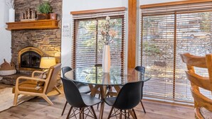 Un salon chaleureux avec une cheminée en pierre, une table en verre entourée de chaises et une vue dégagée grâce à de grandes fenêtres.
