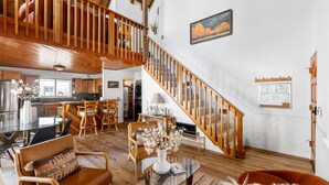 Un vaste espace de vie agrémenté d’un escalier en bois, d’une table à manger avec des chaises, et d’une cuisine en arrière-plan.
