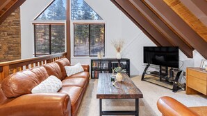 Un salon chaleureux, aménagé dans un style industriel, avec un canapé en cuir, une table basse, un téléviseur et une bibliothèque.