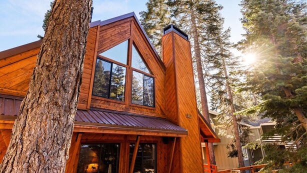 Une cabane en bois dotée de grandes fenêtres, d’un toit en pente et d’une cheminée.