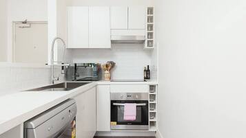 A compact kitchen with white cabinetry, a built-in oven, and a dishwasher.