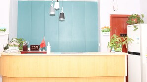 A reception desk with a teal-colored backdrop, a white refrigerator, and potted plants. - One Meter Sunshine Xi'an Xianyang International Airport Hotel (Xianyang)