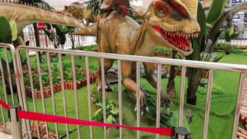 Une exposition sur les dinosaures, avec des modèles très réalistes, entourée de plantes artificielles et délimitée par une barrière métallique.