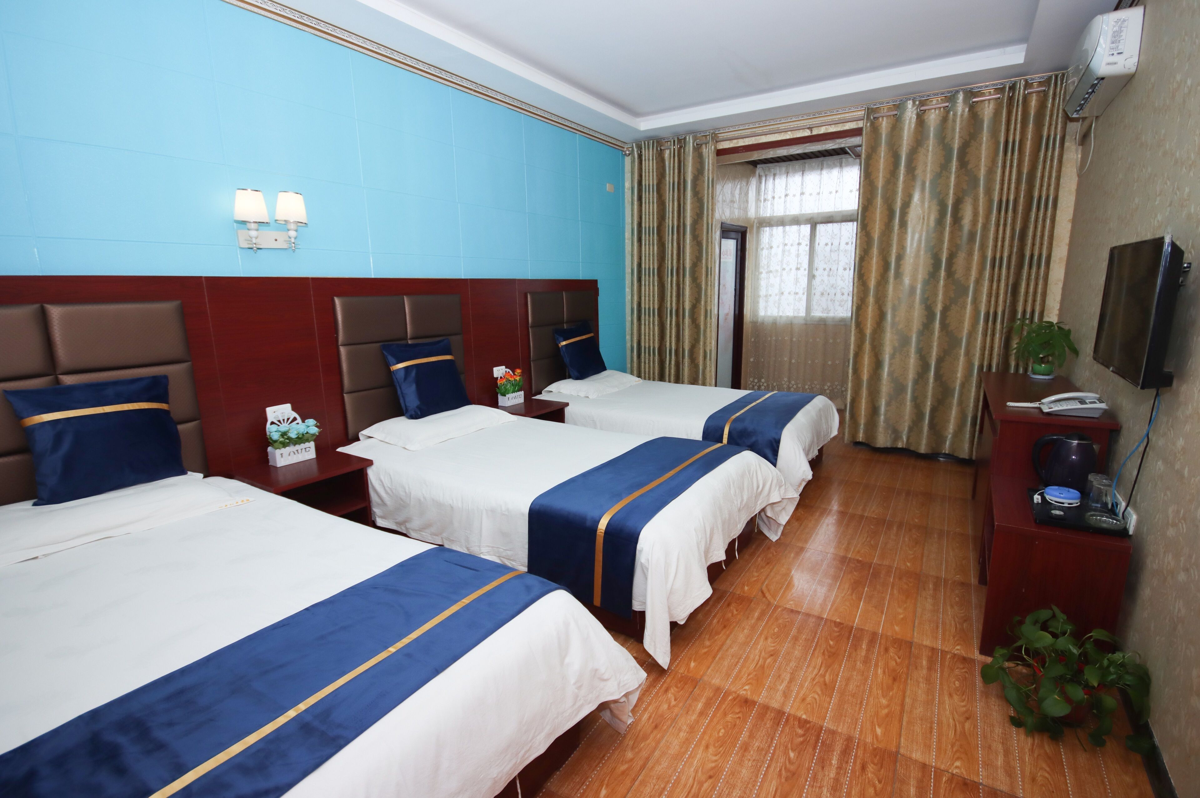 A hotel room with two beds, a wooden floor, a TV, and a window with curtains.