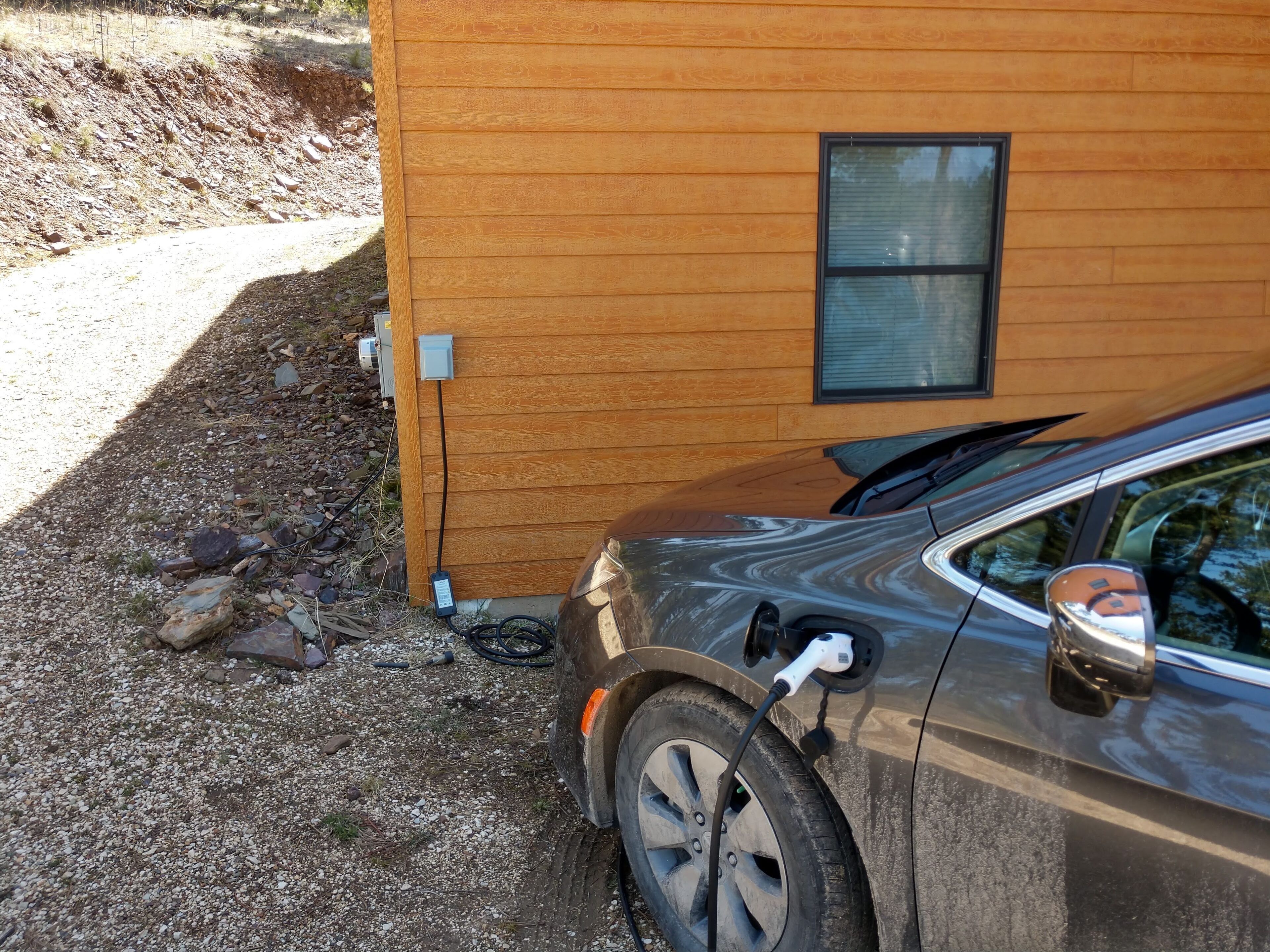 A car parked next to a wooden building with a window and electrical outlets.