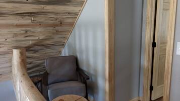 A room with a wooden ceiling, a grey chair, a wooden stool, and a door with a black handle.