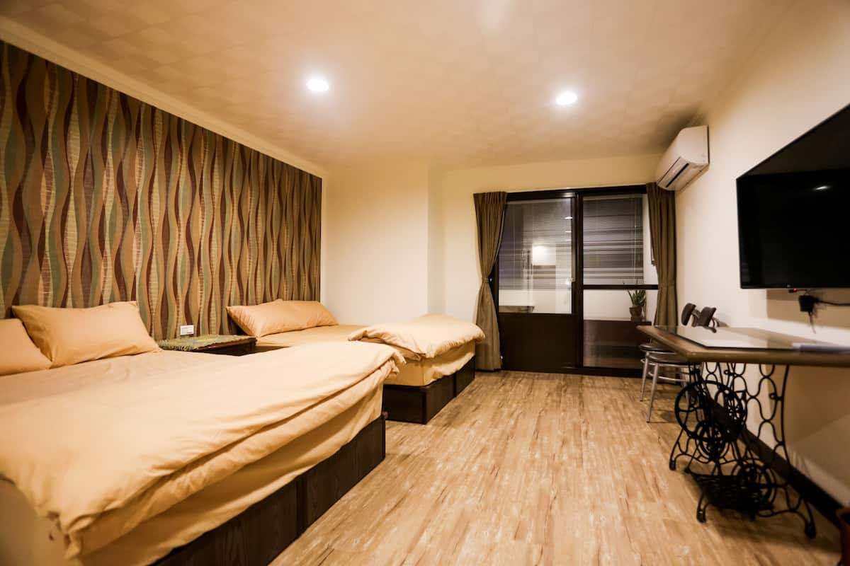 A hotel room with two beds, a desk, a chair, a TV, and a window with blinds.