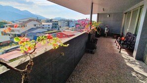 Een balkon met uitzicht op gebouwen en bergen, een bloempot en een bank.