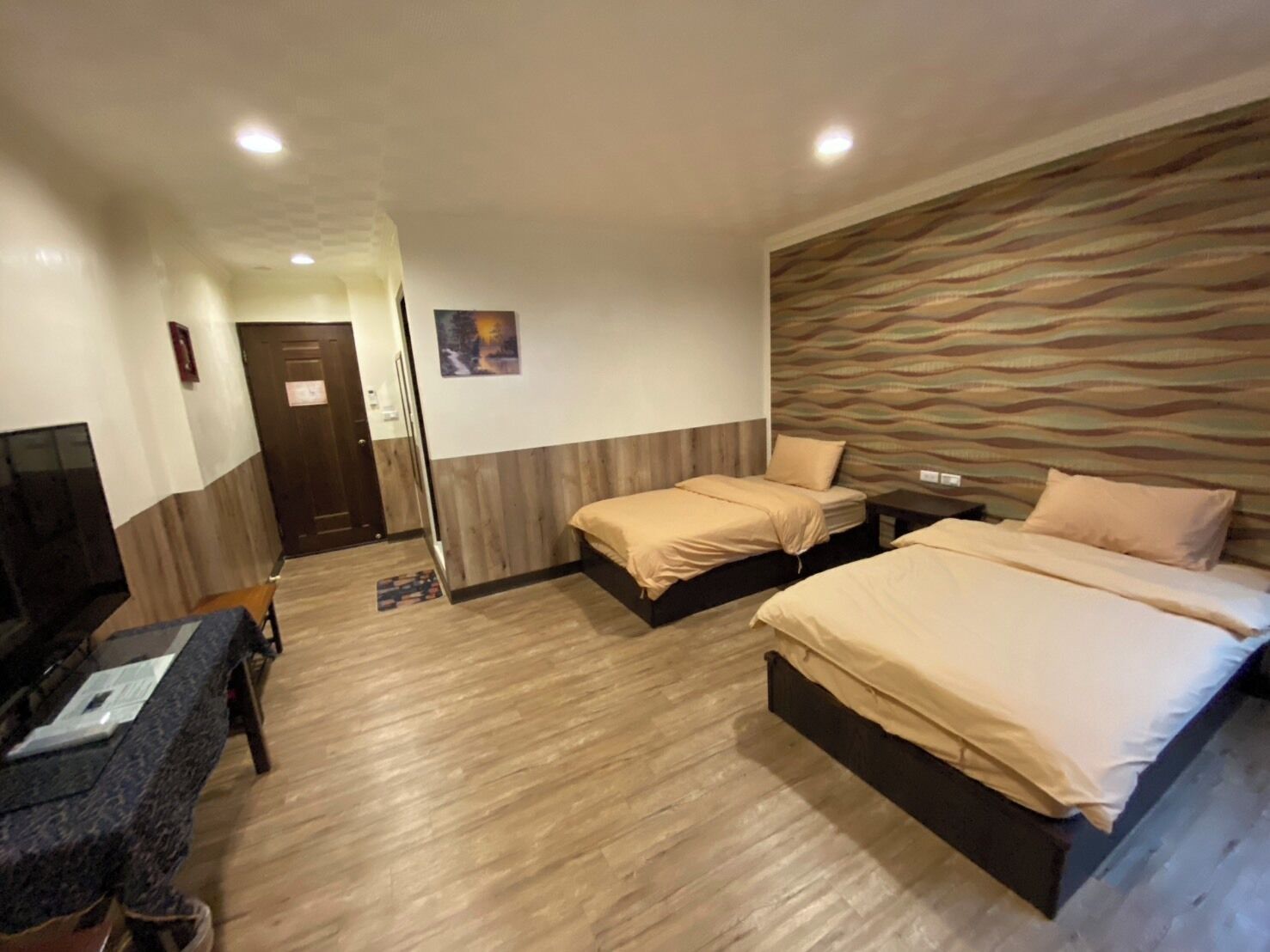 A hotel room with two beds, a desk, a TV, and a wooden floor.