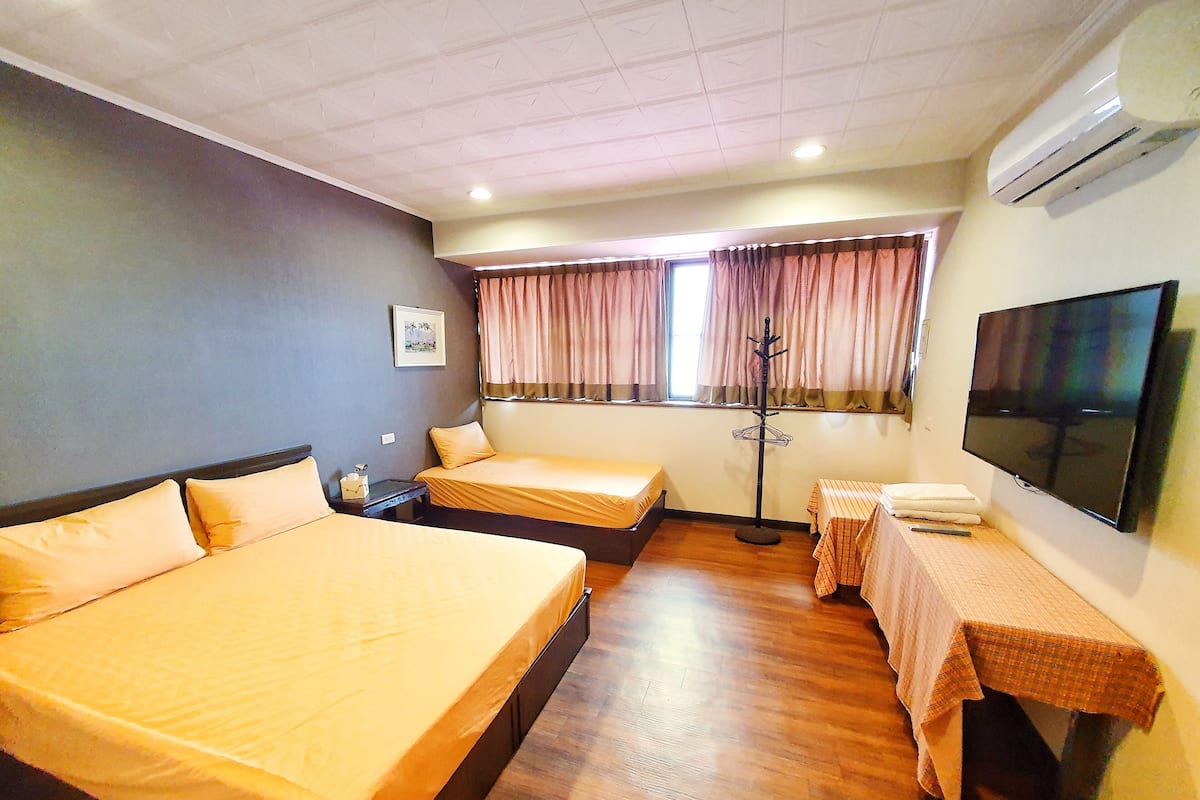 A hotel room with two beds, a TV, a coat rack, and a window with curtains.