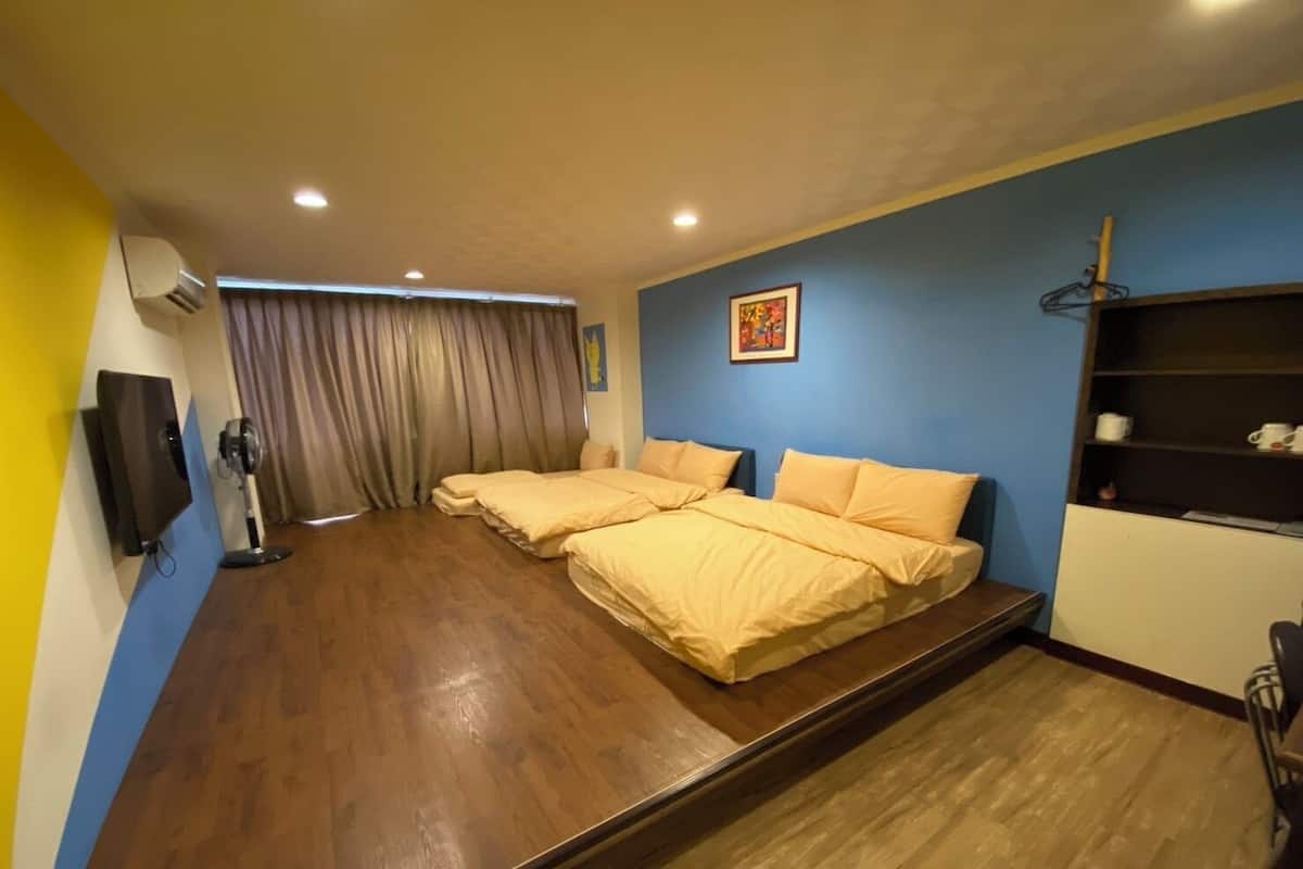 A hotel room with a large bed, a TV, a fan, and a shelf with cups.