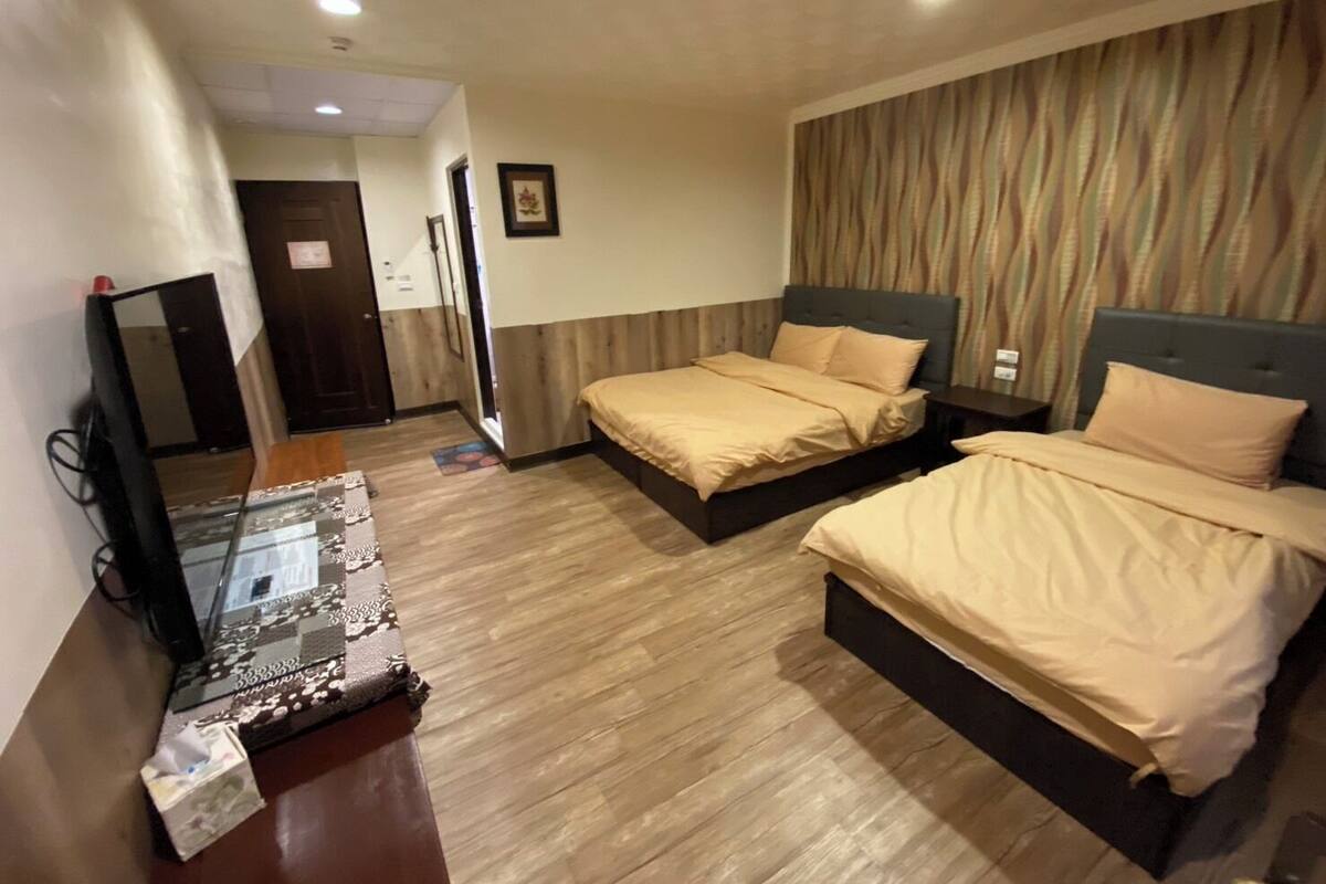A hotel room with two beds, a wooden floor, a television, and a door.