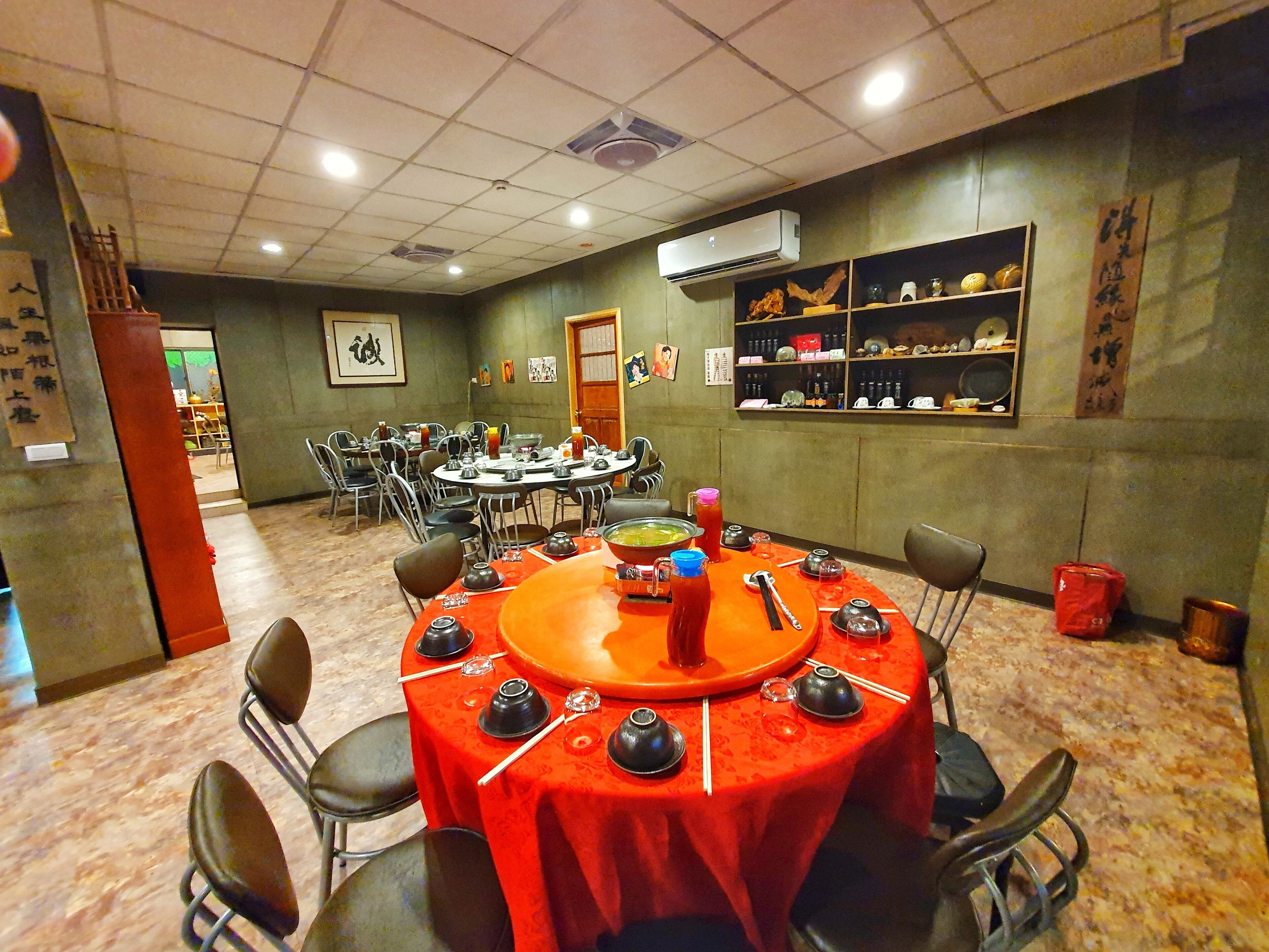 Uma área de refeições com mesas redondas cobertas por toalhas vermelhas, equipada com bules e hashis.