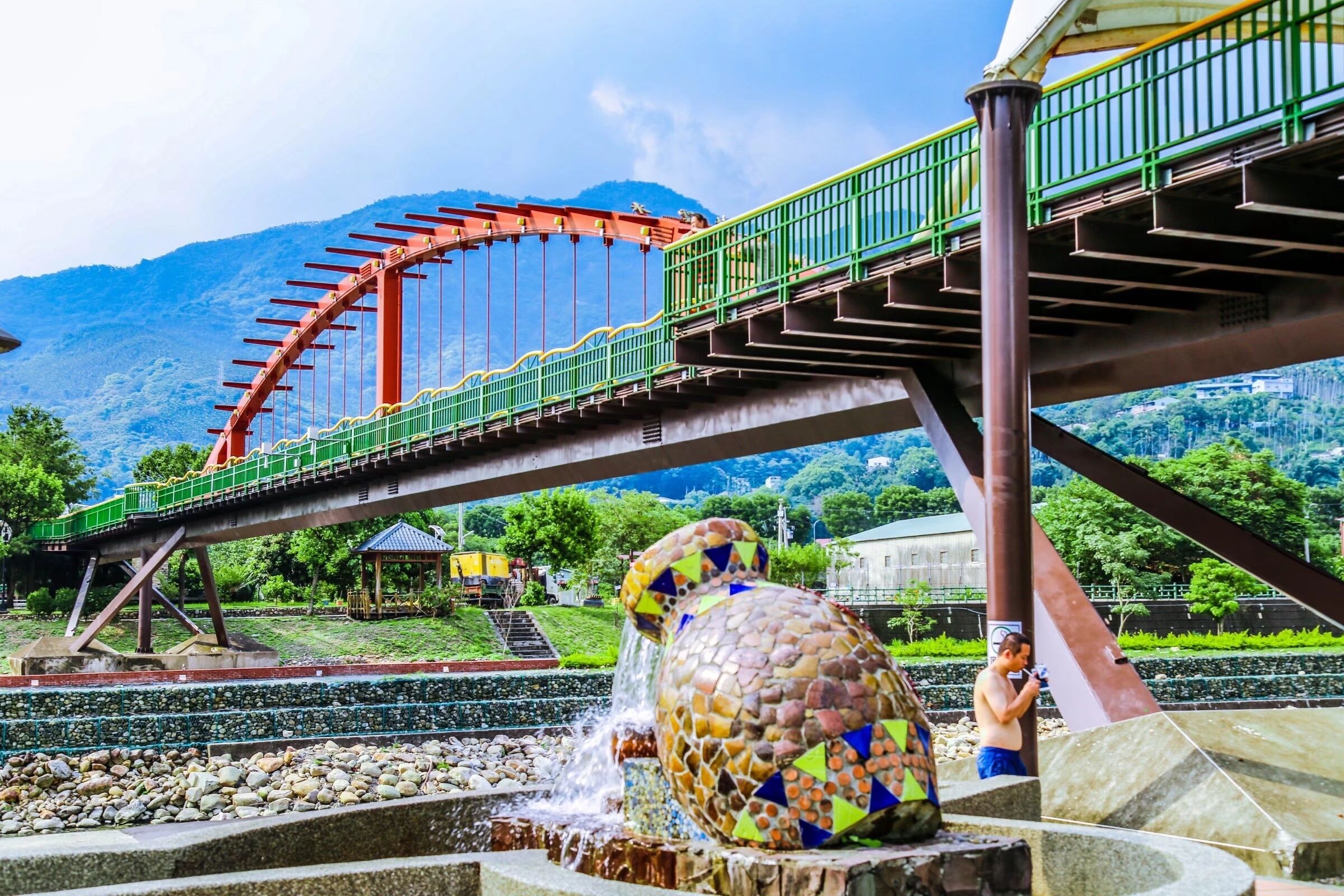 A roller coaster track with a bridge, a mosaic sculpture, and a water feature.