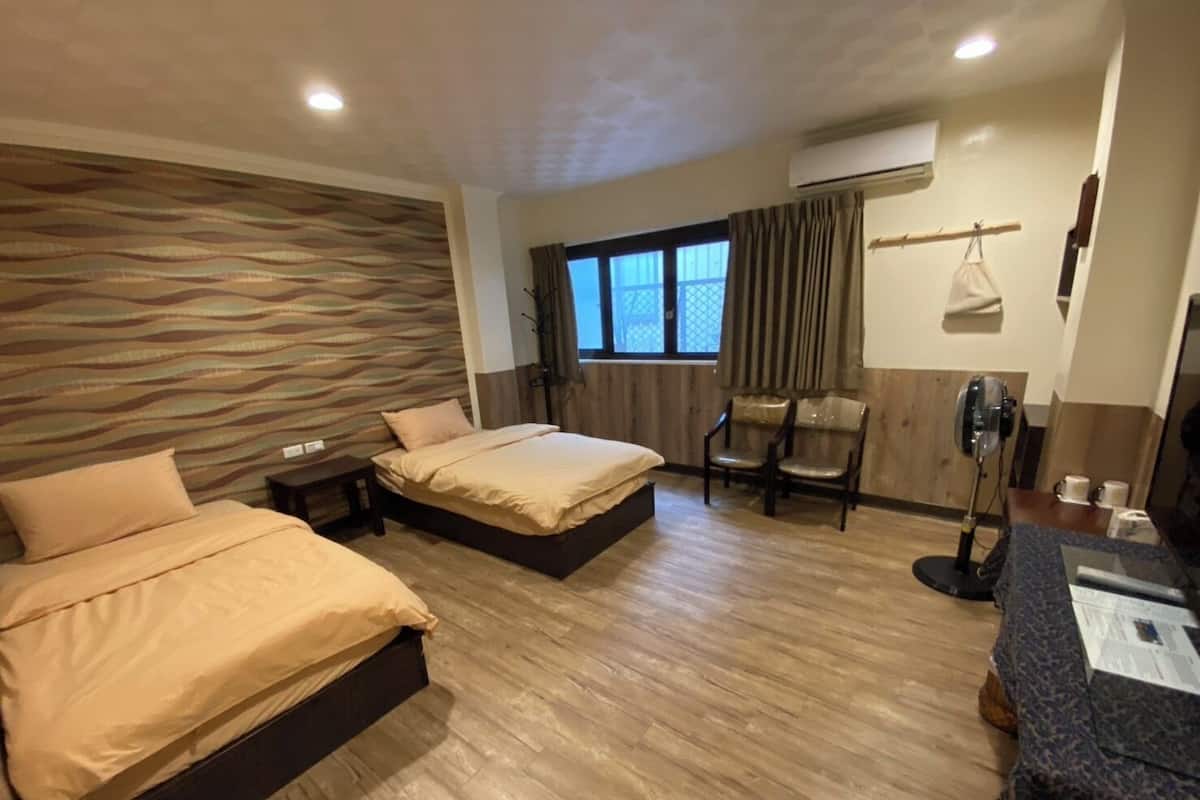 A hotel room with two beds, a desk, a chair, and a window with curtains.