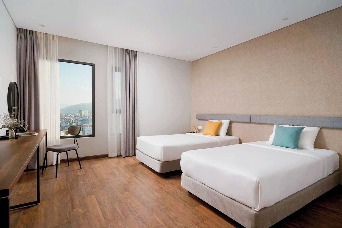 A hotel room with two beds, a desk, and a chair.