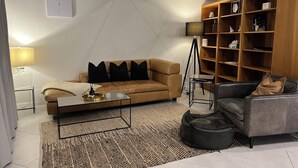 Una sala de estar moderna con un sofá color beige, una mesa de centro, un sillón de cuero negro, una lámpara de pie y una estantería.