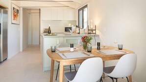Una cocina moderna con armarios blancos, una isla central y un comedor con dos sillas blancas y una mesa de madera.