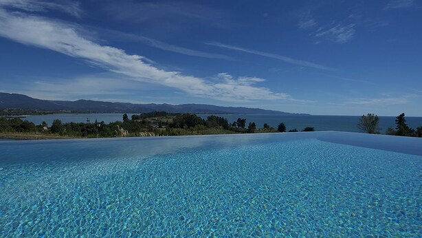 Una piscina infinita de color azul cristalino con vistas a montañas y un lago.