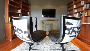 Una habitación con dos cómodos sofás tipo sillón, un televisor de pantalla plana montado en la pared y estanterías de madera llenas de libros.