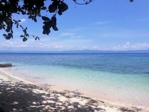 A beach with clear turquoise water, a sandy shore, and distant mountains under a clear sky. - Carolina del Mar (Samboan)
