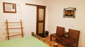 A room with a bed, two wooden chairs, a small table, a wooden ladder, a door with a grid pattern, and a wall-mounted picture frame. - Carolina del Mar (Samboan)