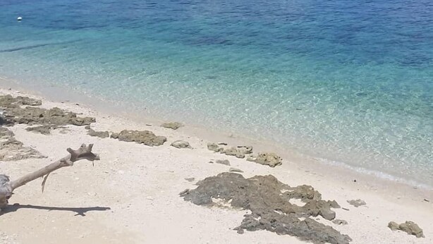 A beach with clear turquoise water, rocky outcrops, and distant mountains under a partly cloudy sky. - Carolina del Mar (Samboan)