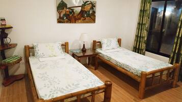 Two beds with floral-patterned bedspreads, a table with a lamp, and a shelf with personal items.