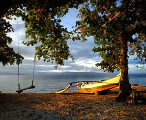 A beach with a hammock and a boat under a tree. - Carolina del Mar (Samboan)