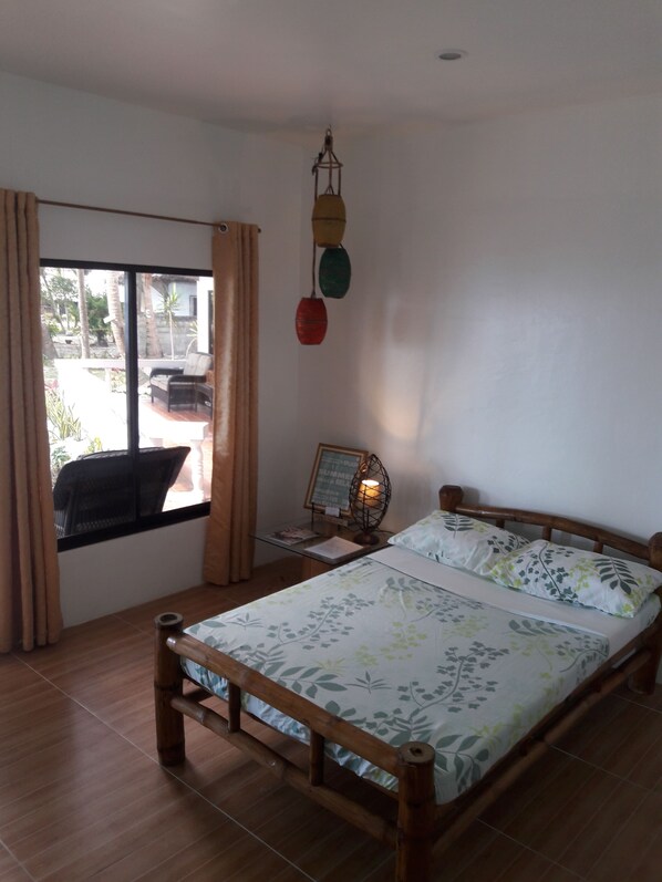 Un dormitorio con cama de madera, ventana con cortinas, mesita de noche con lámpara y vistas al exterior.