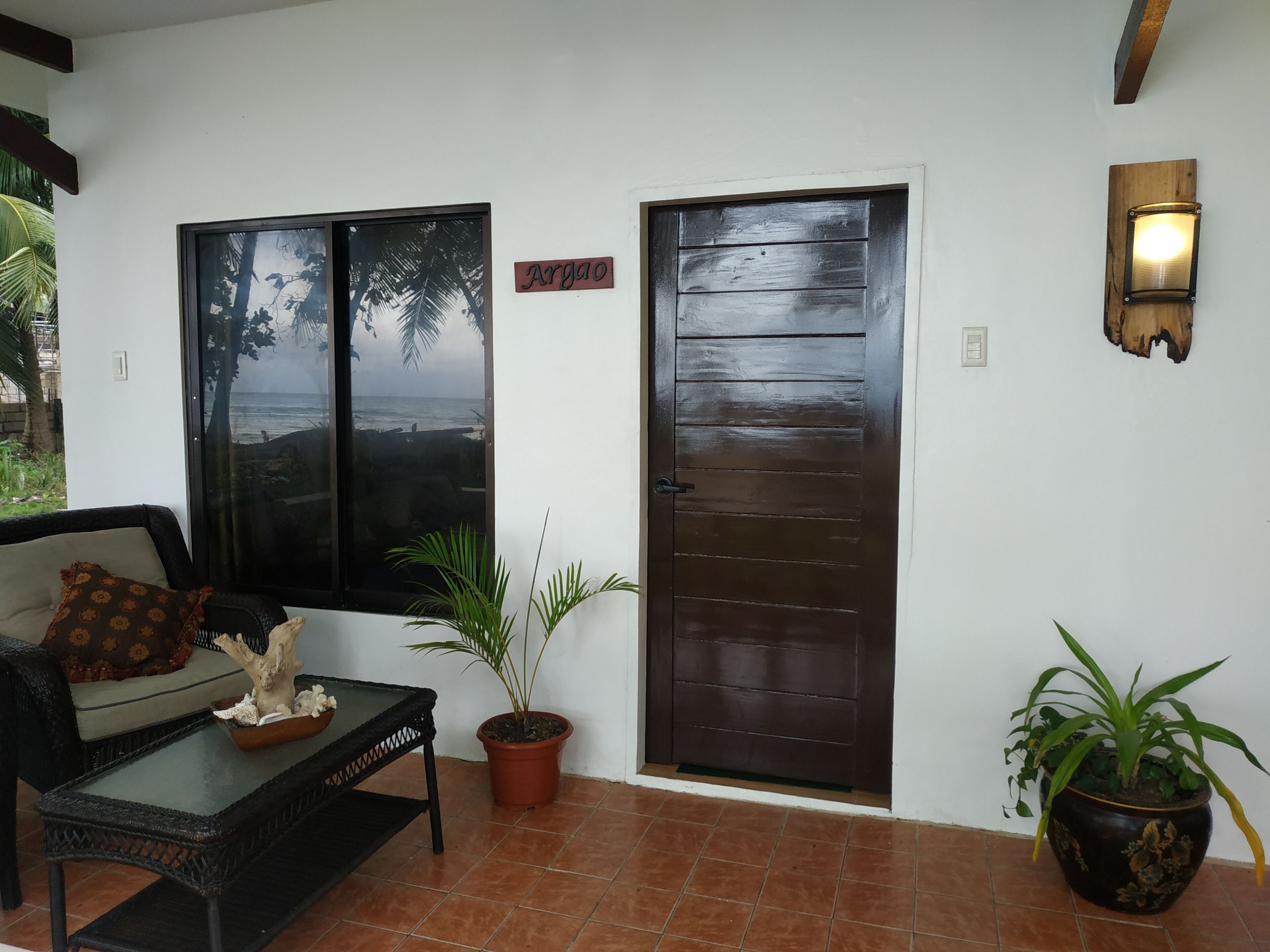 Quarto com sofá, uma mesinha, planta em vaso, porta de madeira e janela com vista para o oceano.