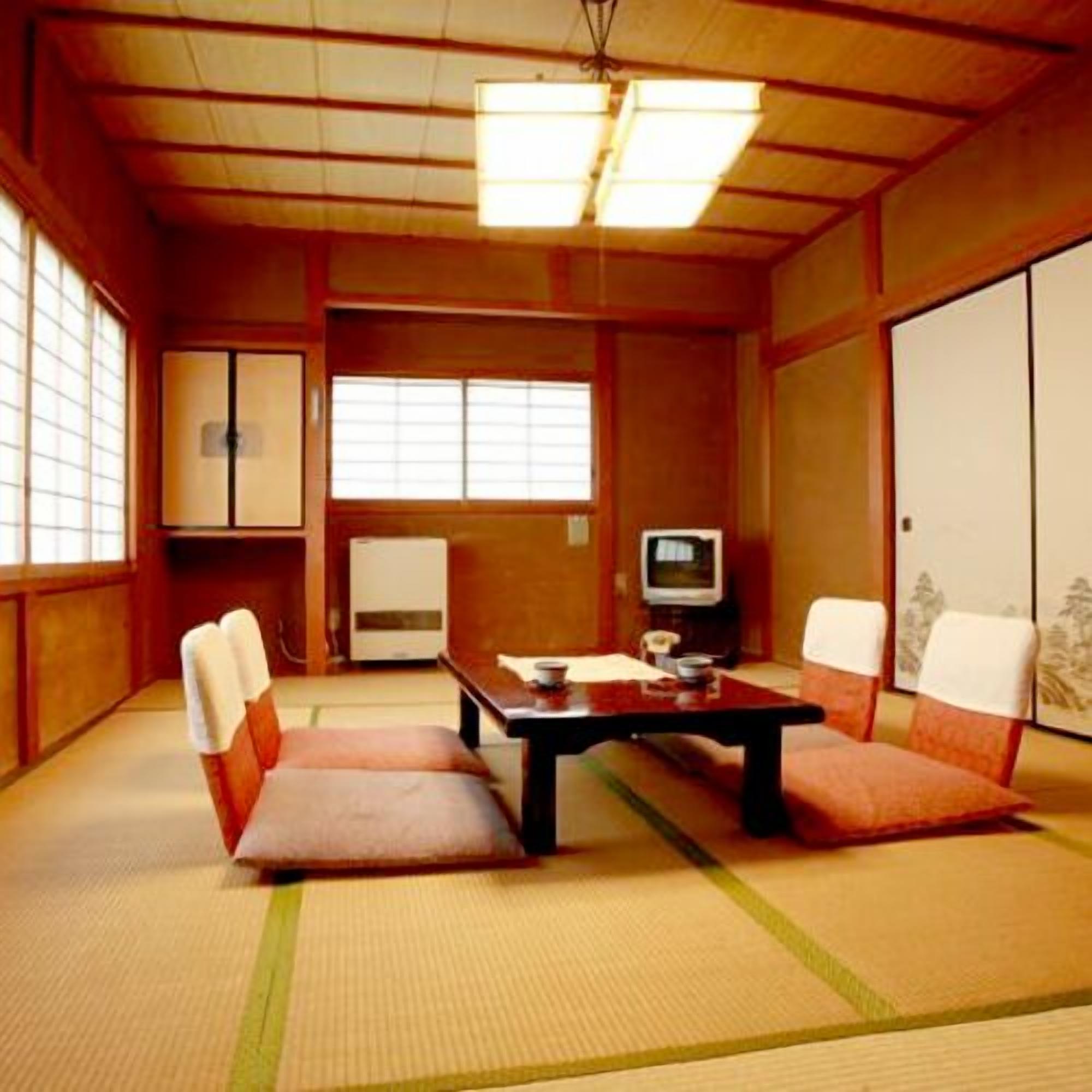 A traditional Japanese room with tatami flooring, a low table, cushions, a television, and sliding doors.