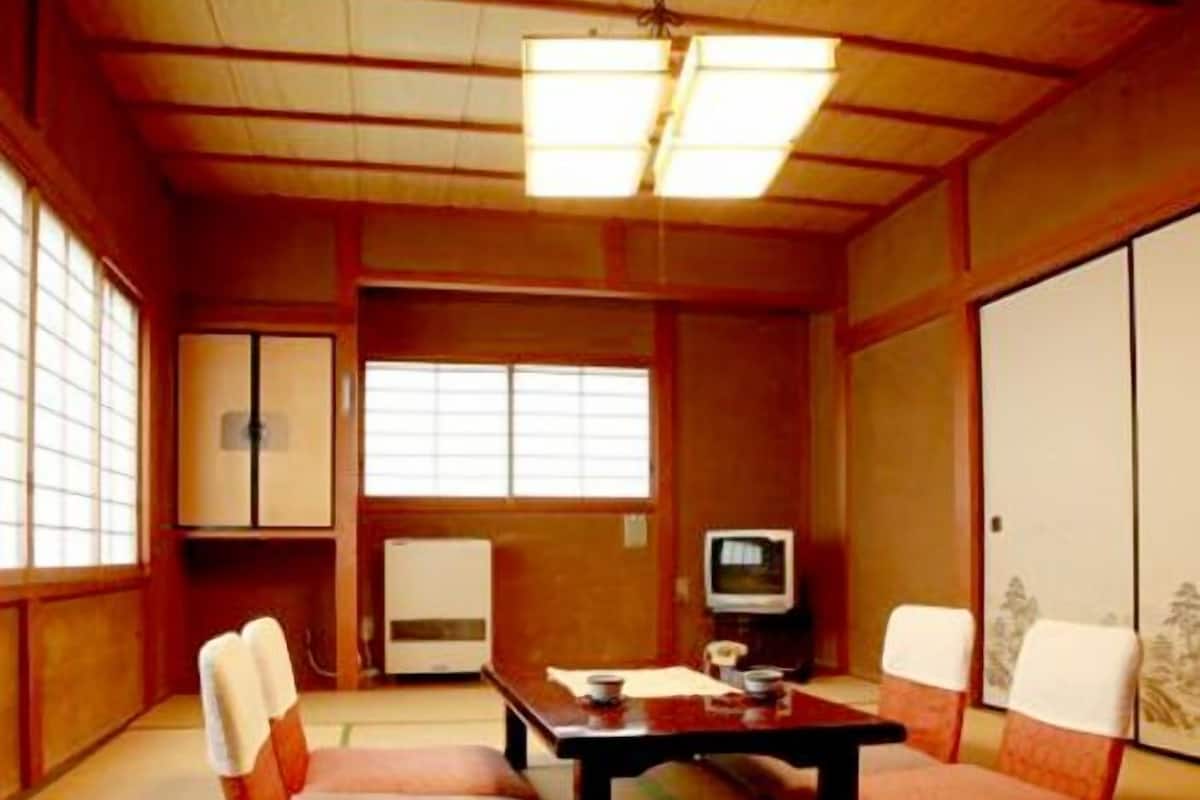 A traditional Japanese room with tatami flooring, a low table, cushions, a television, and sliding doors.