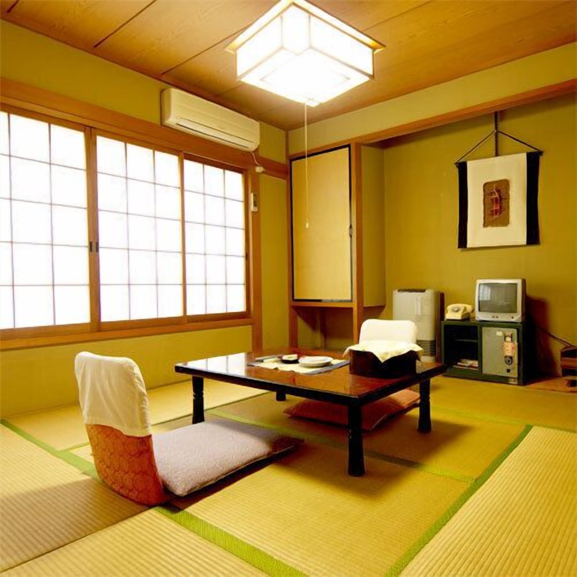 A traditional Japanese room with tatami flooring, a low table, a chair, a television, and a framed picture on the wall.