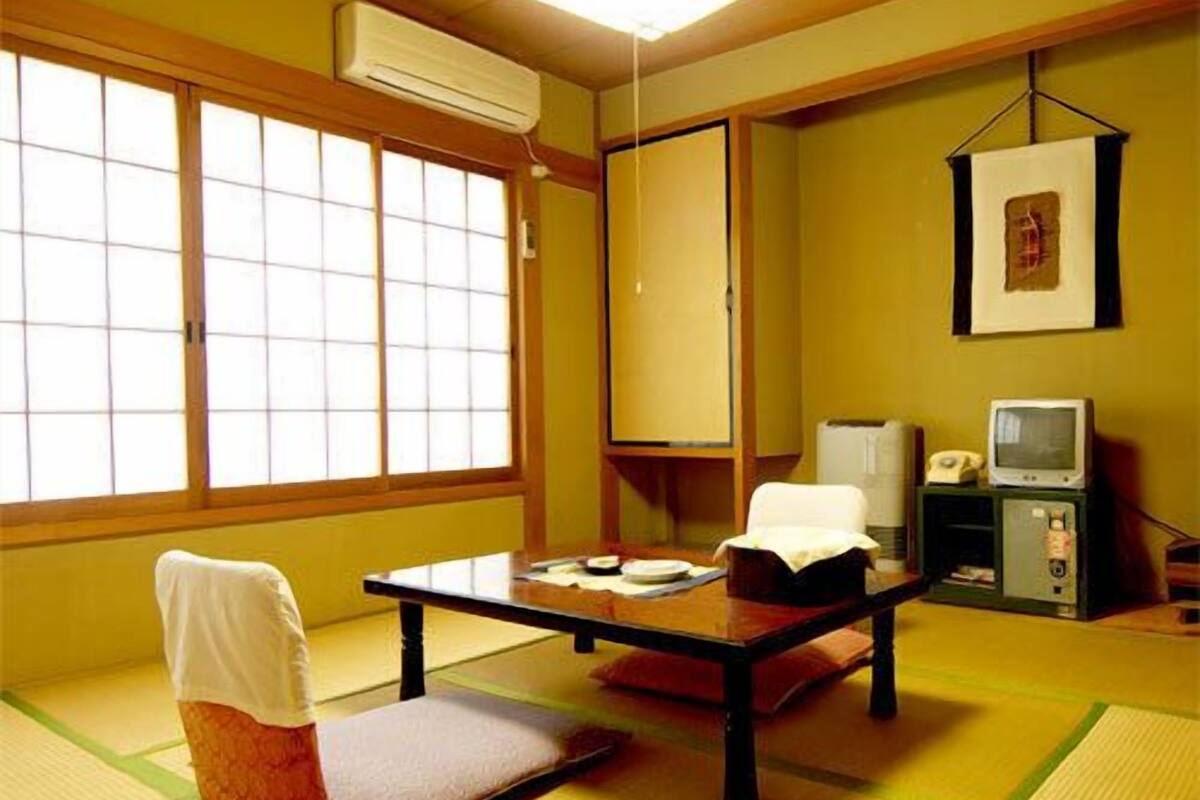 A traditional Japanese room with tatami flooring, a low table, a chair, a television, and a framed picture on the wall.
