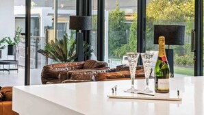 Ein modernes Wohnzimmer mit Glastrennwand, Ledersofa und einem Tisch mit Champagnerflasche und Gläsern.