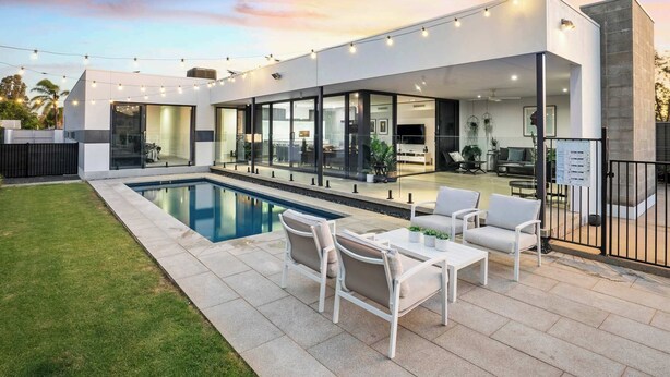 Ein modernes Haus mit Schwimmbad, Sitzgelegenheit im Freien und einer großen Glasdoor, die zum Innenbereich führt.