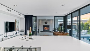 Eine moderne Küche mit einer zentralen Kochinsel, einem Kamin und einer großen Glaswand mit Blick ins Freie.